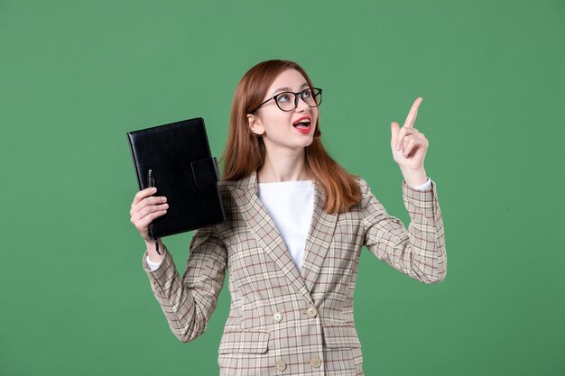 Portrait of female teacher holding notepad on green