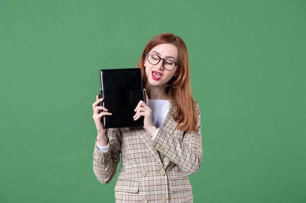 Portrait of female teacher holding notepad on green