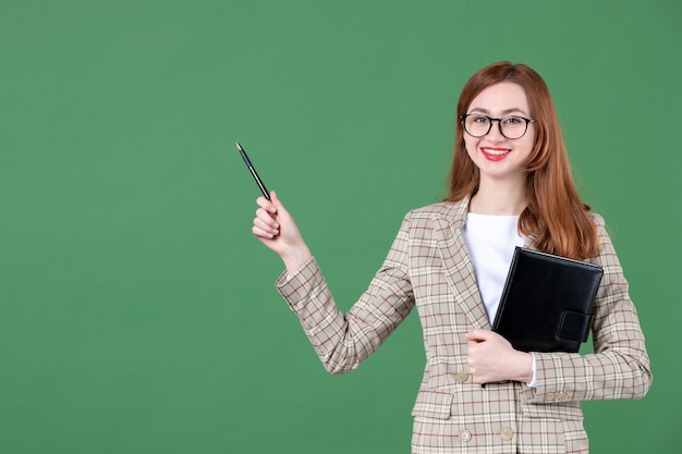 Portrait of female teacher holding notepad on green