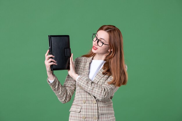 Portrait of female teacher holding notepad on green