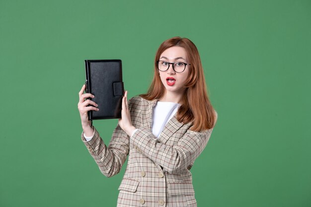 Portrait of female teacher holding notepad on green