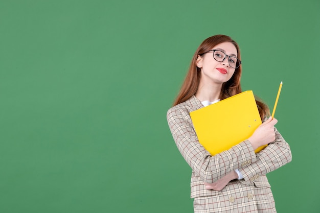 Portrait of female teacher holding yellow document on green