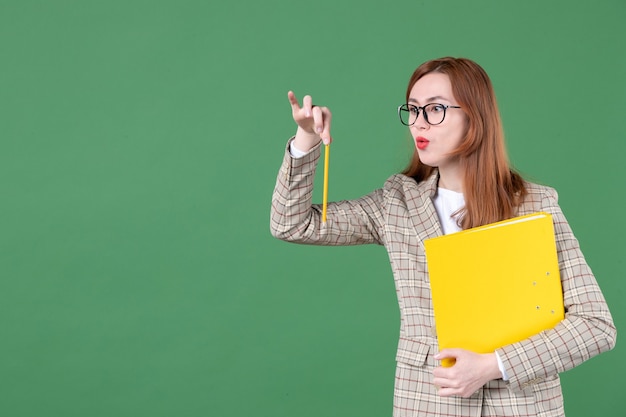 Portrait of female teacher holding yellow document and pencil on green