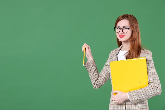 Portrait of female teacher holding yellow document and smiling on green