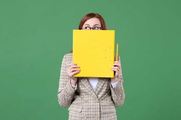 Free photo portrait of female teacher holding yellow files on green