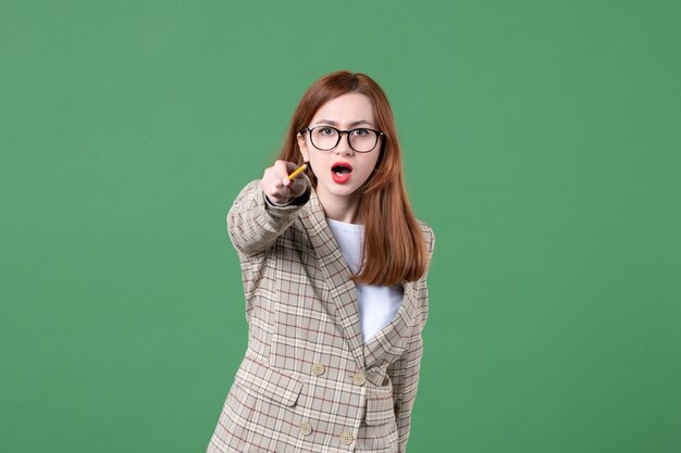 Portrait of female teacher pointing with pencil on green