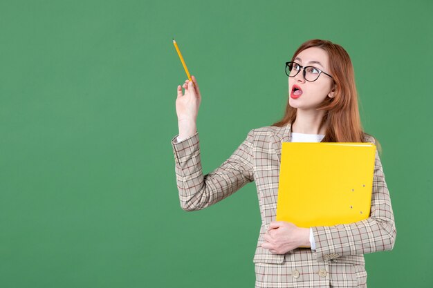 Portrait of female teacher posing with yellow file on green