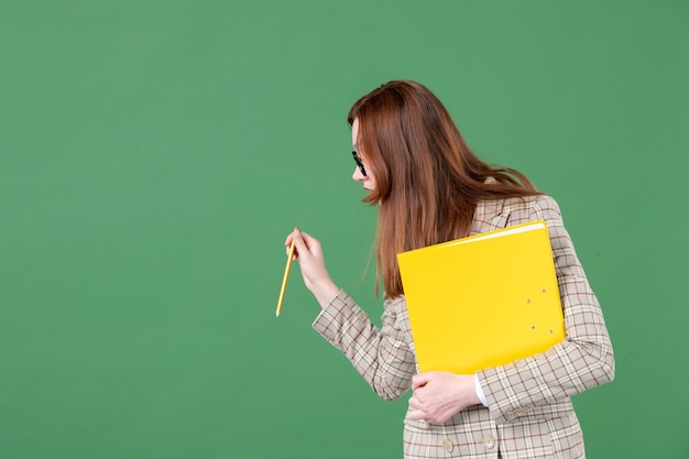 Portrait of female teacher posing with yellow file on green