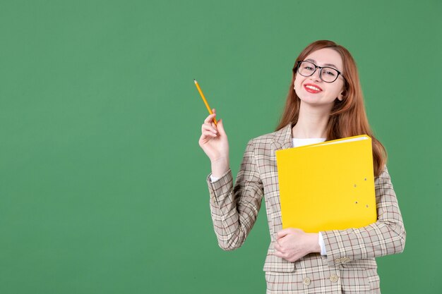 Portrait of female teacher posing with yellow file and pencil on green