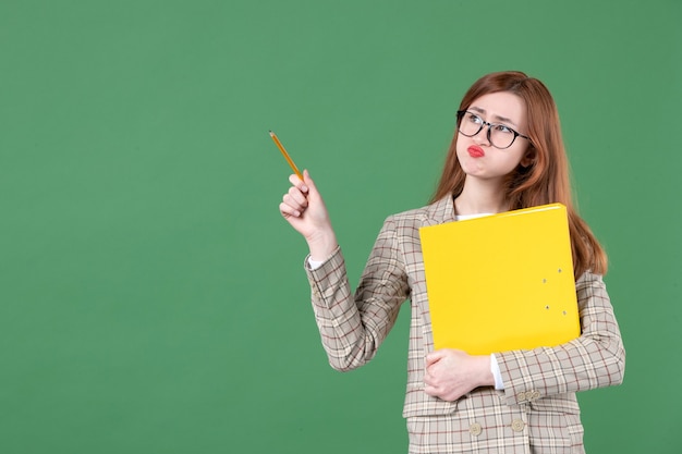 Portrait of female teacher posing with yellow file and pencil on green