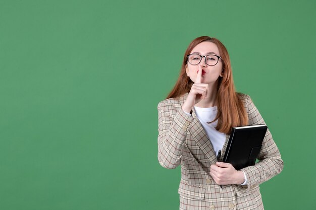 Portrait of female teacher with notepad asking to be silent on green