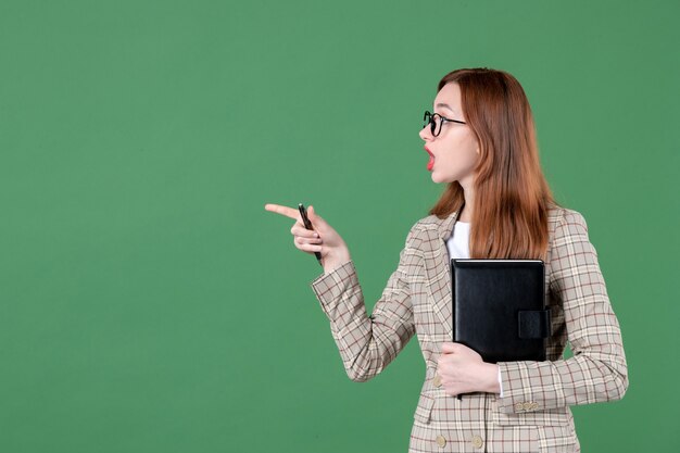 Portrait of female teacher with notepad on green