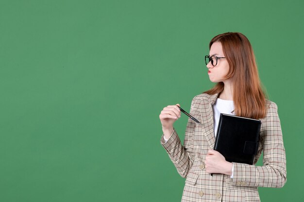 Portrait of female teacher with notepad on green