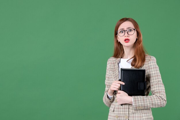 Portrait of female teacher with notepad on green