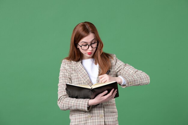 Portrait of female teacher with notepad and pen on green