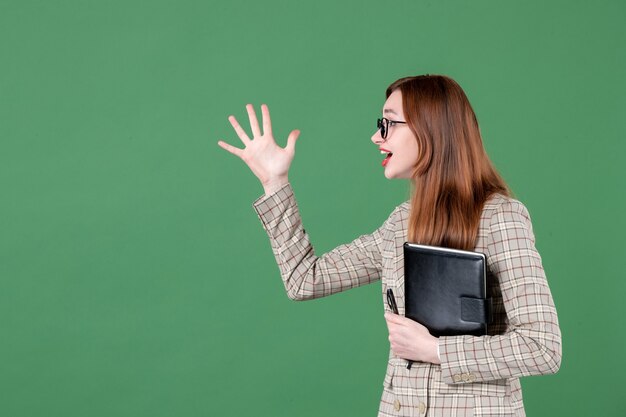 Portrait of female teacher with notepad talking to someone on green