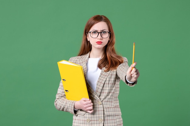 Portrait of female teacher with yellow files angry on green