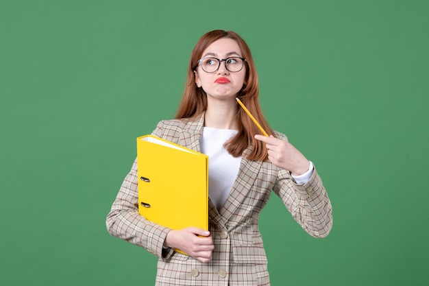 Free photo portrait of female teacher with yellow files on green