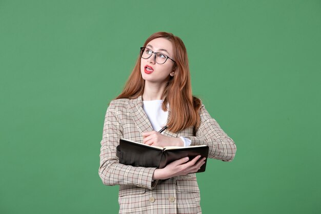 Portrait of female teacher writing down notes on green