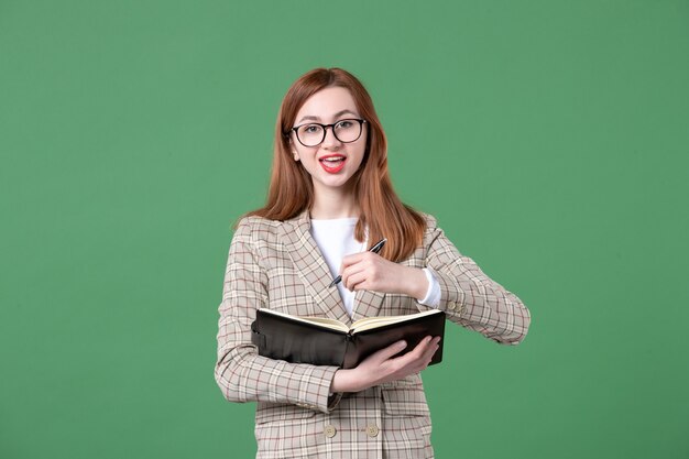 Portrait of female teacher writing down notes on green