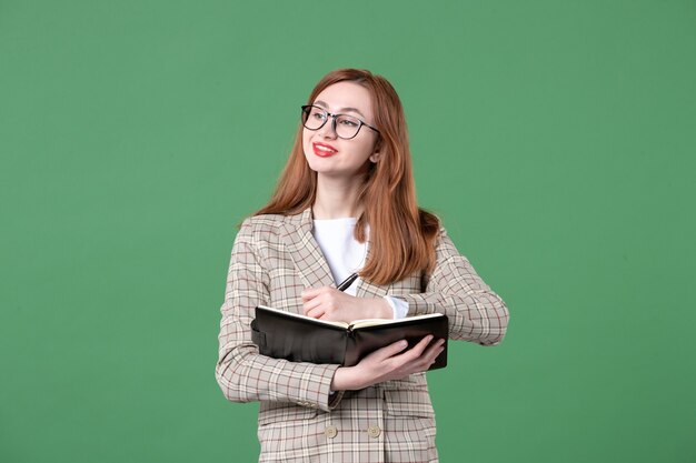 Portrait of female teacher writing down notes on green