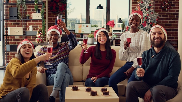 Portrait of festive coworkers clinking glasses with alcohol to celebrate christmas holiday time with toast or cheers. People celebrating winter festivity event with wine beverage in decorated office.