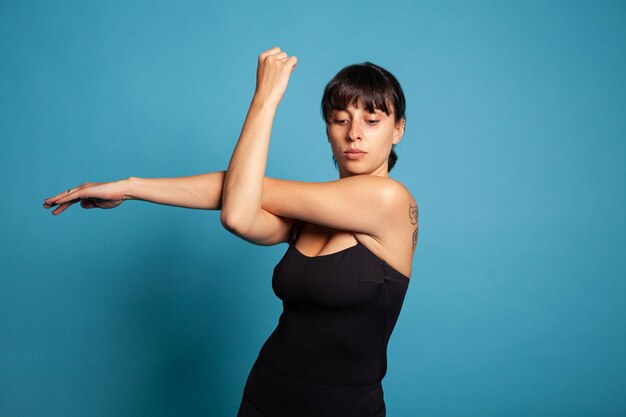 Портрет подтянутой активной женщины, растягивающей мышцы рук, тренирующей выносливость тела во время фитнес-тренировки. Личный тренер в спортивной одежде, практикующий упражнения на растяжку, работающий над здоровым образом жизни