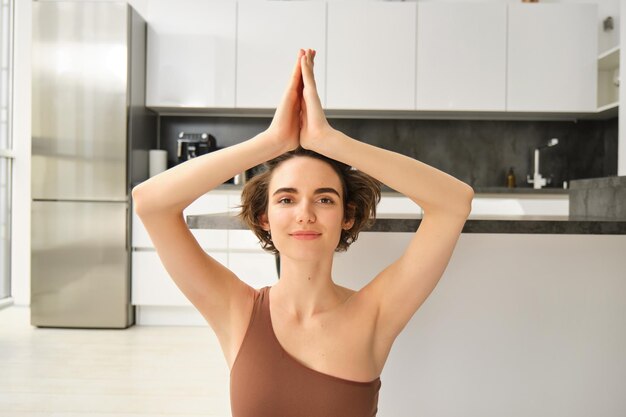 Portrait of fit and healthy woman in sportswear doing yoga at home on fitness mat making asana relax