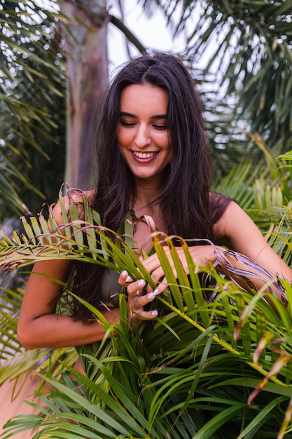 Portrait of fit tanned slim woman in green tiny bikini posing with tropical leaves