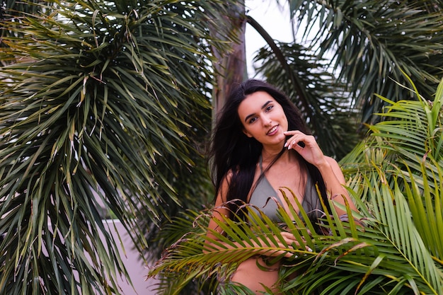 Portrait of fit tanned slim woman in green tiny bikini posing with tropical leaves