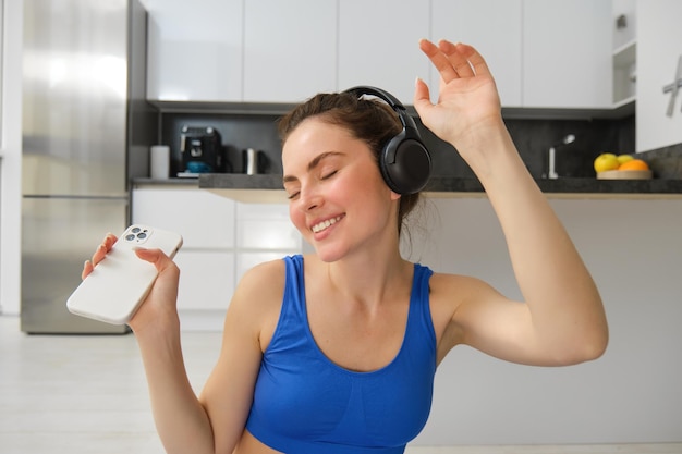 Free photo portrait of fitness instructor woman with headphones and smartphone dancing at home workout inside