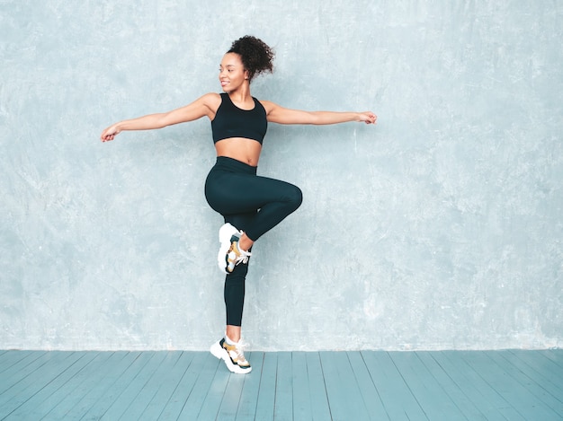 Portrait of fitness smiling woman in sports clothing with afro curls hairstyle