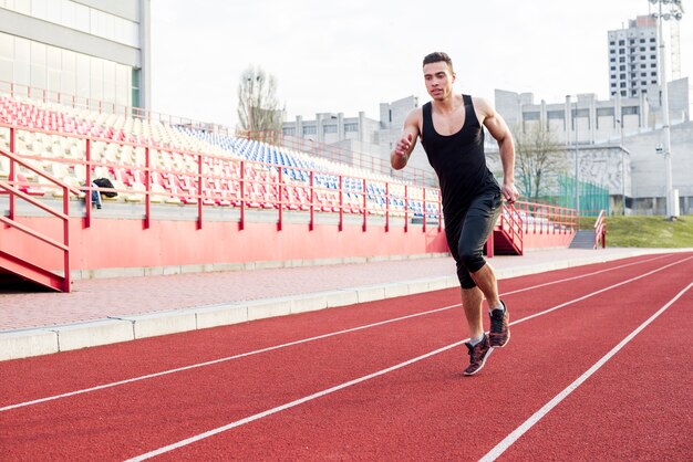 Portrait of fitness young male athlete running on race track in the stadium