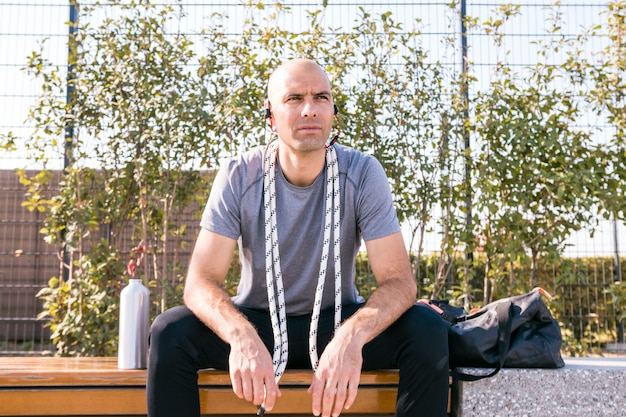 Free photo portrait of a fitness young man sitting on bench with rope around his neck looking away