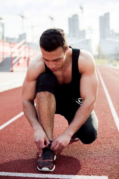 Free photo portrait of fitness young man tying shoelace on track field