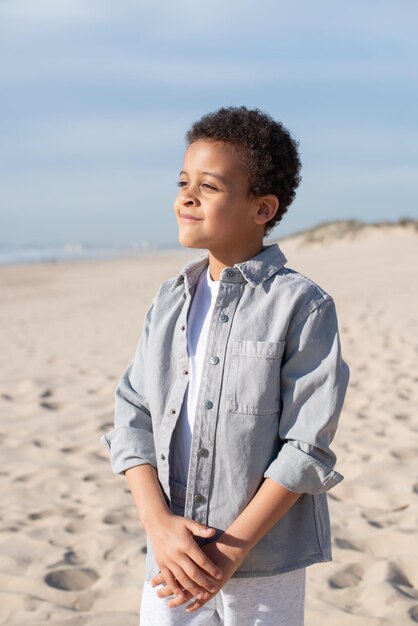 ビーチに焦点を当てたアフリカ系アメリカ人の少年の肖像画。カジュアルな服装で巻き毛の男性モデルが横向きにポーズをとっています。肖像画、美しさの概念