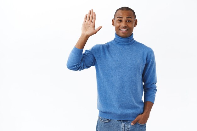 Portrait of friendly charismatic young african-american man saying hi to people at work, raising hand and waving it hello