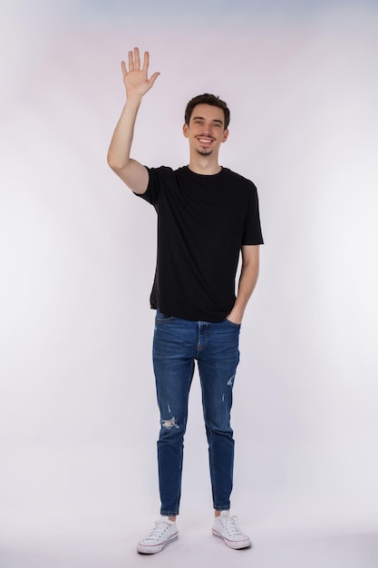 Портрет дружелюбного жизнерадостного мужчины в черной футболке и джинсах, говорящего приветствую человека, машущего рукой