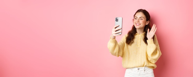 Portrait of friendly girl talking on video chat app waving hand at smartphone camera having mobile c