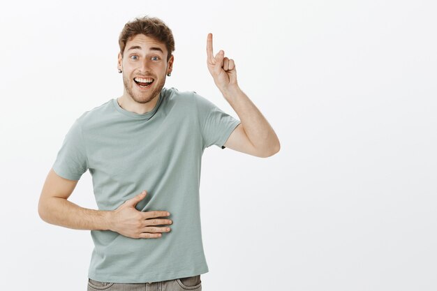 Portrait of friendly good-looking Caucasian man with bristle and fair hair, raising index finger and pointing up