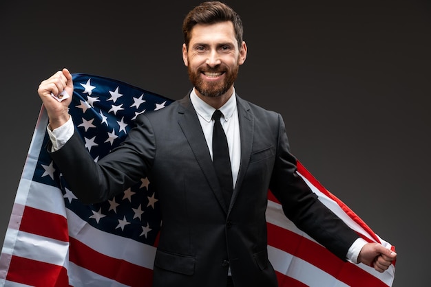 Portrait of friendly pretty man smiling broadly and holding flag of america. elections day and business cooperation concept. indoor studio shot isolated on black background
