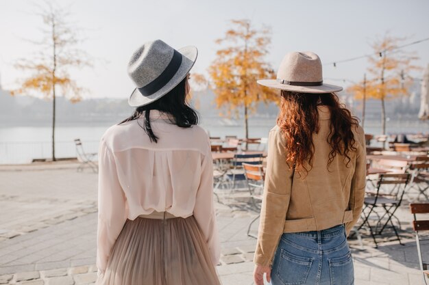 Portrait from back of brunette woman in hat talking with friend on nature