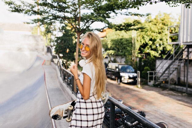 Portrait from back of caucasian girl holding skateboard and laughing.