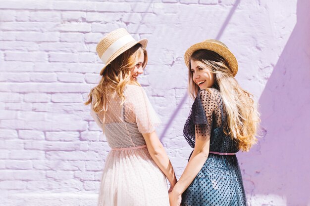 Portrait from back of elegant girls in straw summer hats joking and laughing