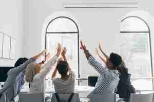 Free photo portrait from back of tired students stretching after long work. indoor photo of office workers fooling around during meeting in conference hall with big windows.