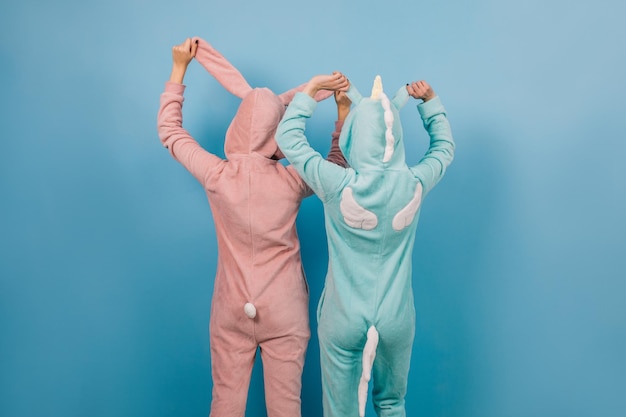 Free photo portrait from back of young ladies in kigurumi relaxed girls posing on blue background in pajamas