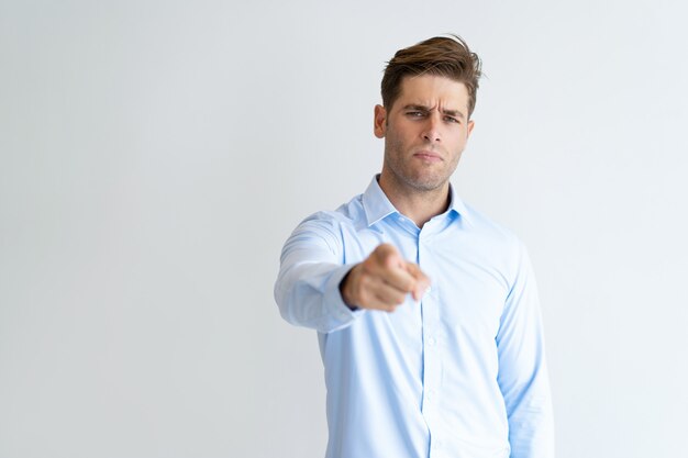 Portrait of frowning businessman pointing at camera with finger