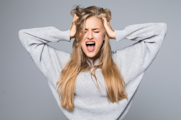 Ritratto di una donna arrabbiata frustrata che grida ad alta voce e tirando fuori i capelli isolato su sfondo grigio