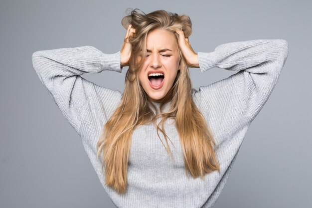 Portrait of a frustrated angry woman screaming out loud and pulling her hair out isolated on the gray background