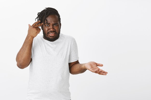 Portrait of frustrated guy with braids posing against the white wall